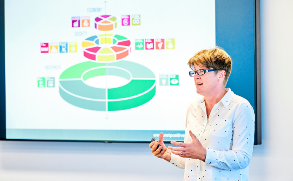 A lecturer discusses the sustainable development goals in a lecture with a screen with a diagram in the background